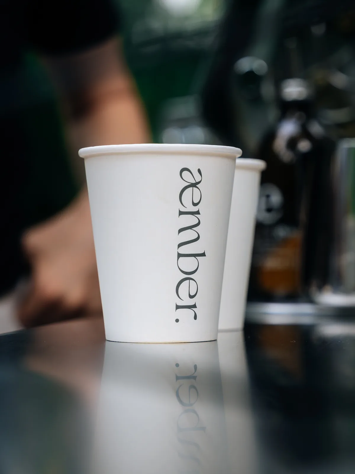 æmber.-Becher mit Spiegelung auf der Edelstahltheke